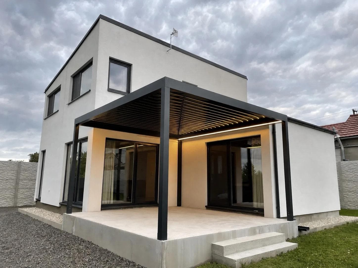 Hotová bioklimatická pergola Panorea KAYA s osvetlenými lamelami pri modernom rodinnom dome